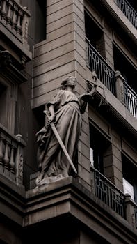 A sculpture of Lady Justice with a sword and scales on a city building's facade.
